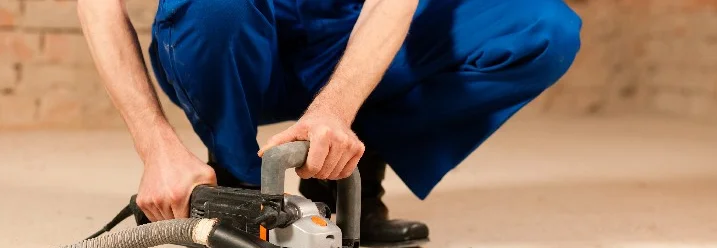 Person schleift Estrich mit Schleifmaschine